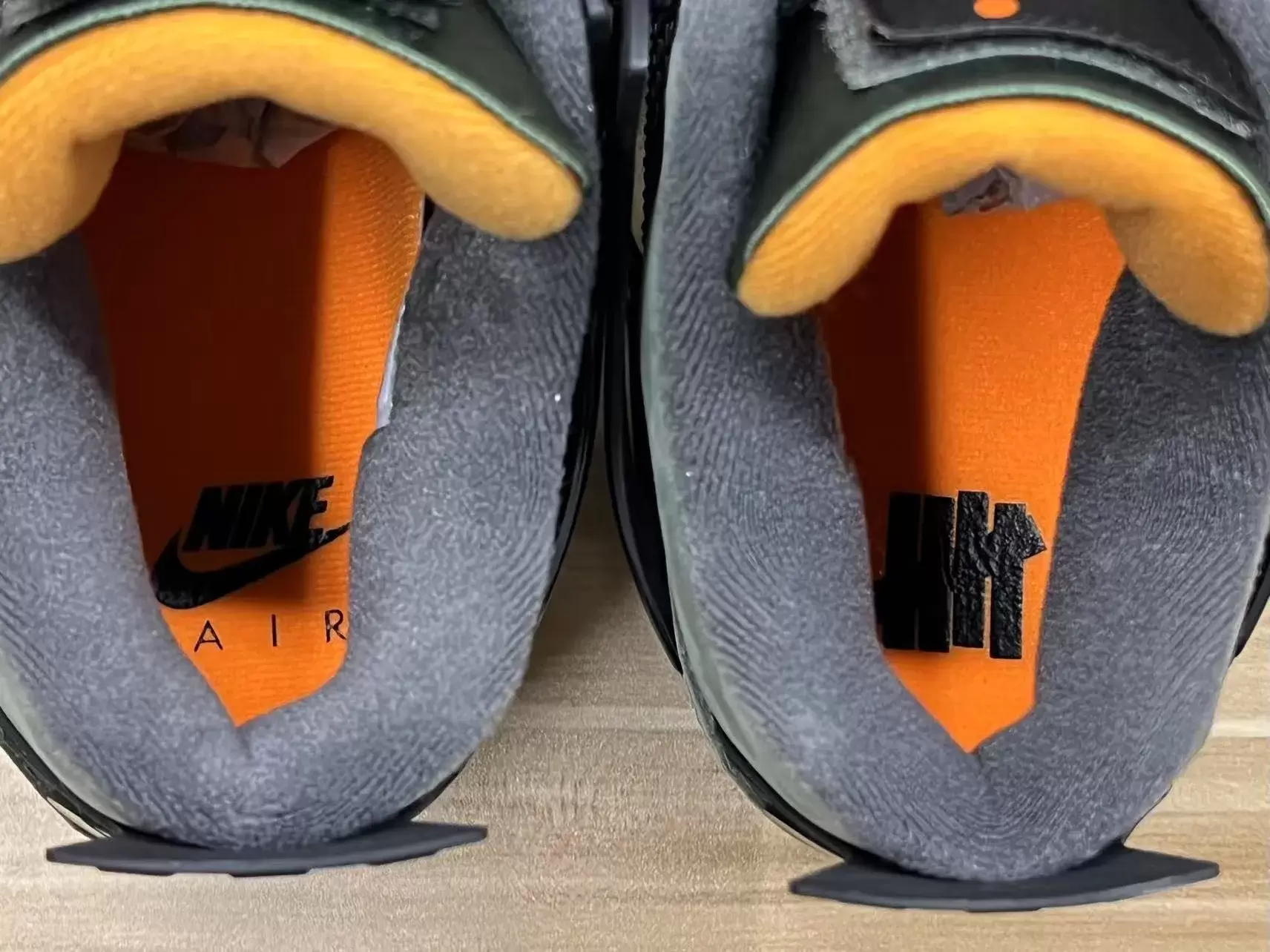 Top-down view of the Undefeated x Air Jordan 4 insoles showing Nike Air and UNDFTD logos on orange footbeds. Top-down view of the Undefeated x Air Jordan 4 insoles showing Nike Air and UNDFTD logos on orange footbeds.