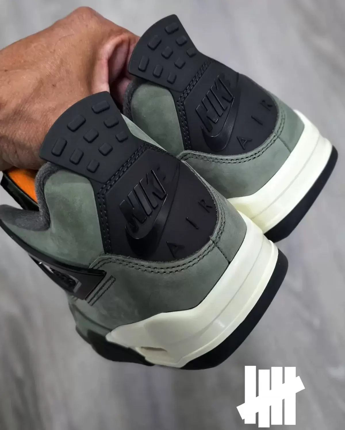 Back view of the 2025 Undefeated x Air Jordan 4 featuring Nike Air heel branding and military green suede Back view of the 2025 Undefeated x Air Jordan 4 featuring Nike Air heel branding and military green suede