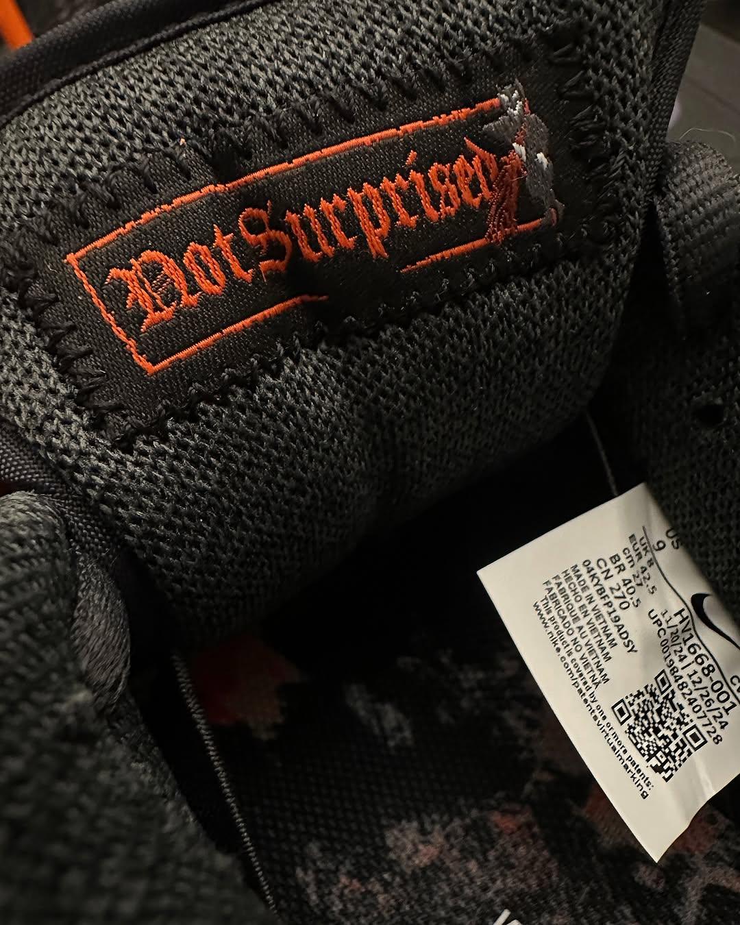 Close-up of the inside tongue tag of the Nike SB Dunk Low Krampus HV1668-001. The tag features the phrase Not Surprised embroidered in red gothic-style font with a small Krampus figure on black fabric. Close-up of the inside tongue tag of the Nike SB Dunk Low Krampus HV1668-001. The tag features the phrase Not Surprised embroidered in red gothic-style font with a small Krampus figure on black fabric.